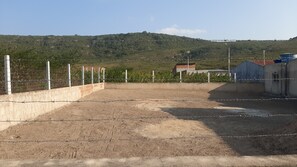 Ein von Zäunen umgebener Außenbereich mit Erdboden, umgeben von einer Betonmauer und einem Metallzaun, mit einer hügeligen Landschaft im Hintergrund.