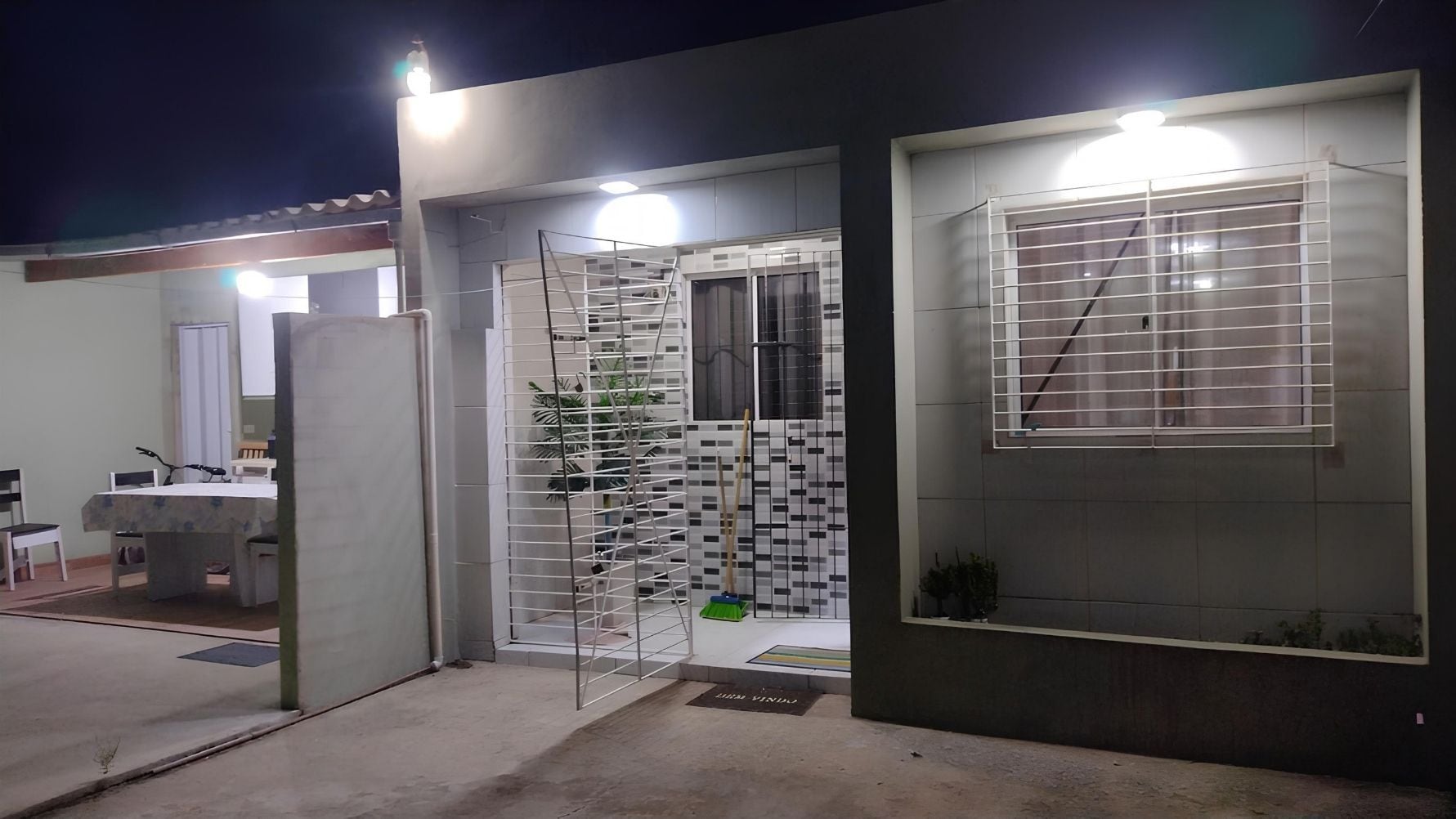A modern exterior with a gated entrance, a small outdoor seating area, and a visible window with a metal grille.