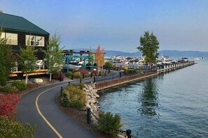 A waterfront walkway with a building on the left, a dock with boats, and a clear sky. - Central Chamberlands Cabin! Pool & Beach Access! (Homewood)