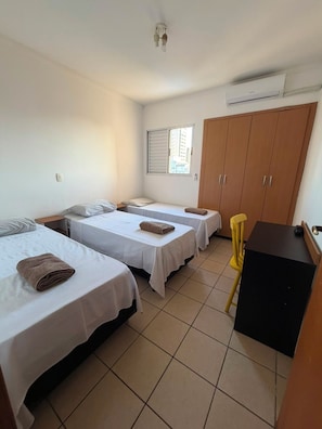 A hotel room with two single beds, a wooden wardrobe, a small table, and a window with blinds. - Residencial Ibis (Bauru)