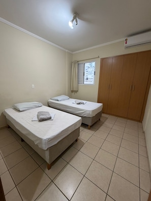 Een kamer met twee enkele bedden, een raam met gordijnen, een kledingkast en een plafondventilator.