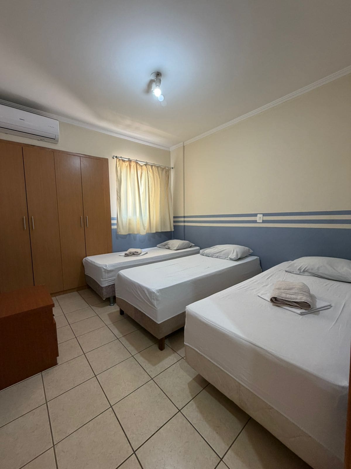Ein Hotelzimmer mit zwei Einzelbetten, einem Holzschrank, einem Schreibtisch und einem Fenster mit Vorhängen.