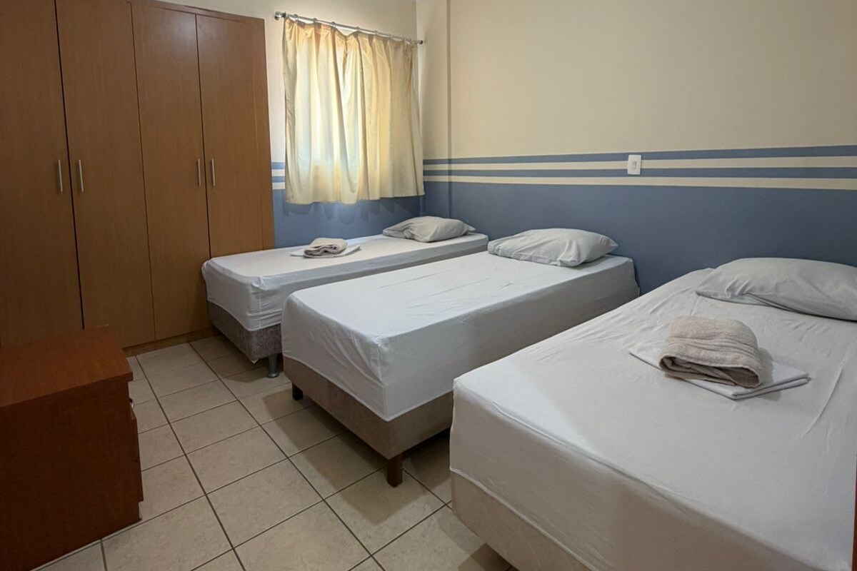 Habitación de hotel con dos camas individuales, un armario de madera, un escritorio y una ventana con cortinas.