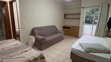 A room with a bed, a sofa, a dining table with chairs, a ceiling fan, and a window with curtains.