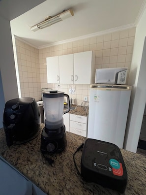 A kitchen with a microwave, toaster, blender, and a coffee maker on the counter. - Residencial Ibis (Bauru)