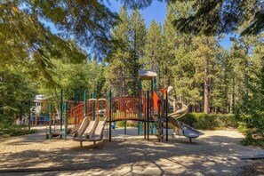 A playground with slides and climbing structures surrounded by trees. - Aidenn’s Cabin - Walk to Tahoe Park Private Beach! (Tahoe City)