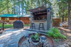 Ein rustikaler Außenbereich mit Bar, Grill, Sitzgelegenheiten und einem Feuerkorb.