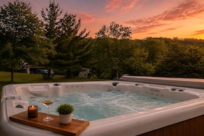Ein Whirlpool mit einer Holzterrasse, einer Kerze und einem Glas Wein.