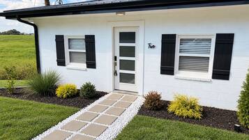 Una casa de un piso con fachada blanca, contraventanas negras y un cartel con el número Dos sobre la puerta.