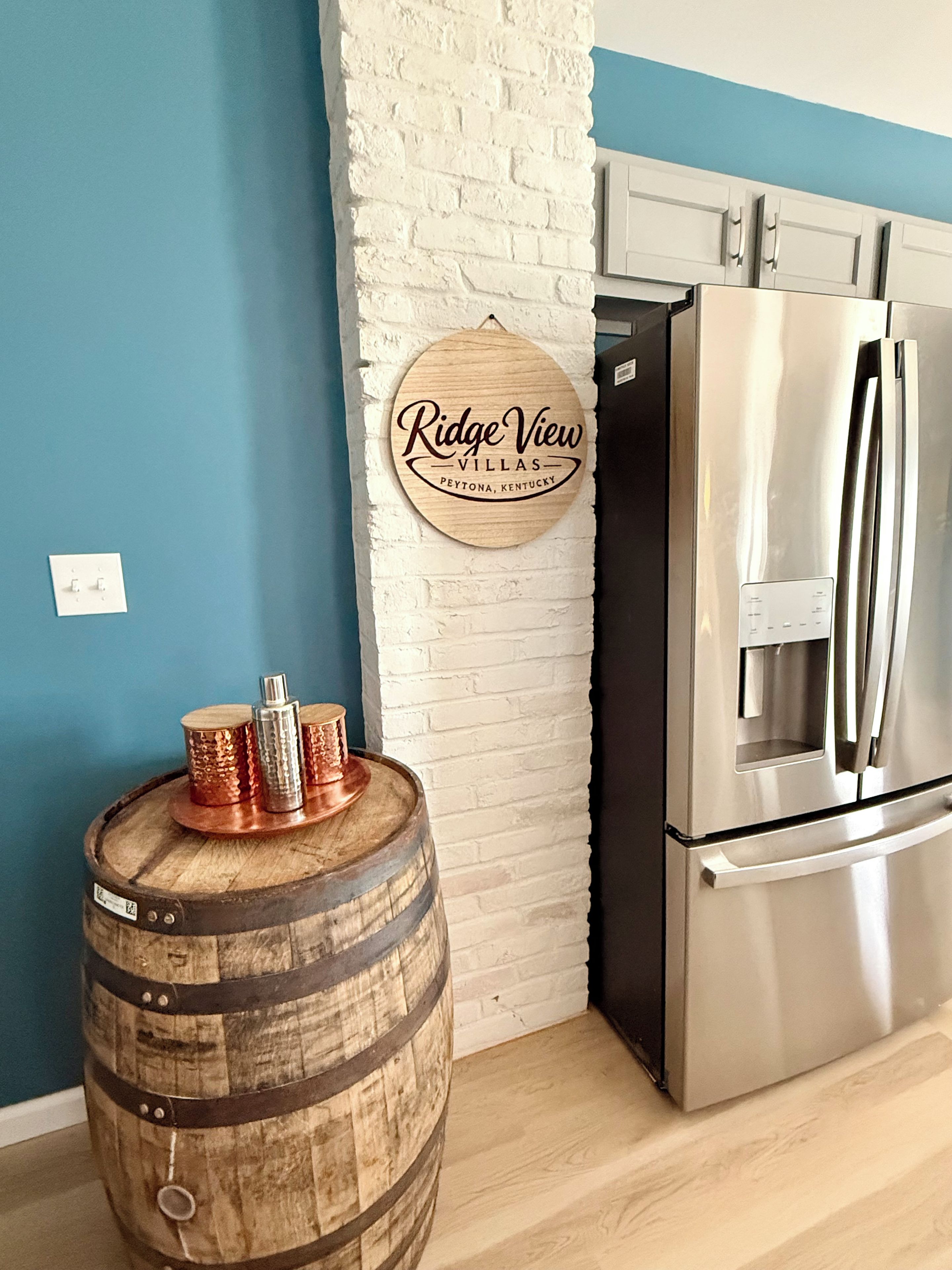 Una cocina con un refrigerador de acero inoxidable, un barril de madera y un cartel en la pared.