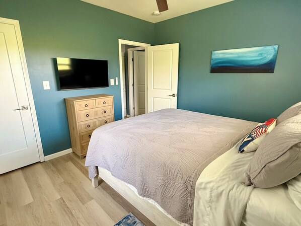 Un dormitorio con cama, cómoda, televisor y obras de arte en la pared.