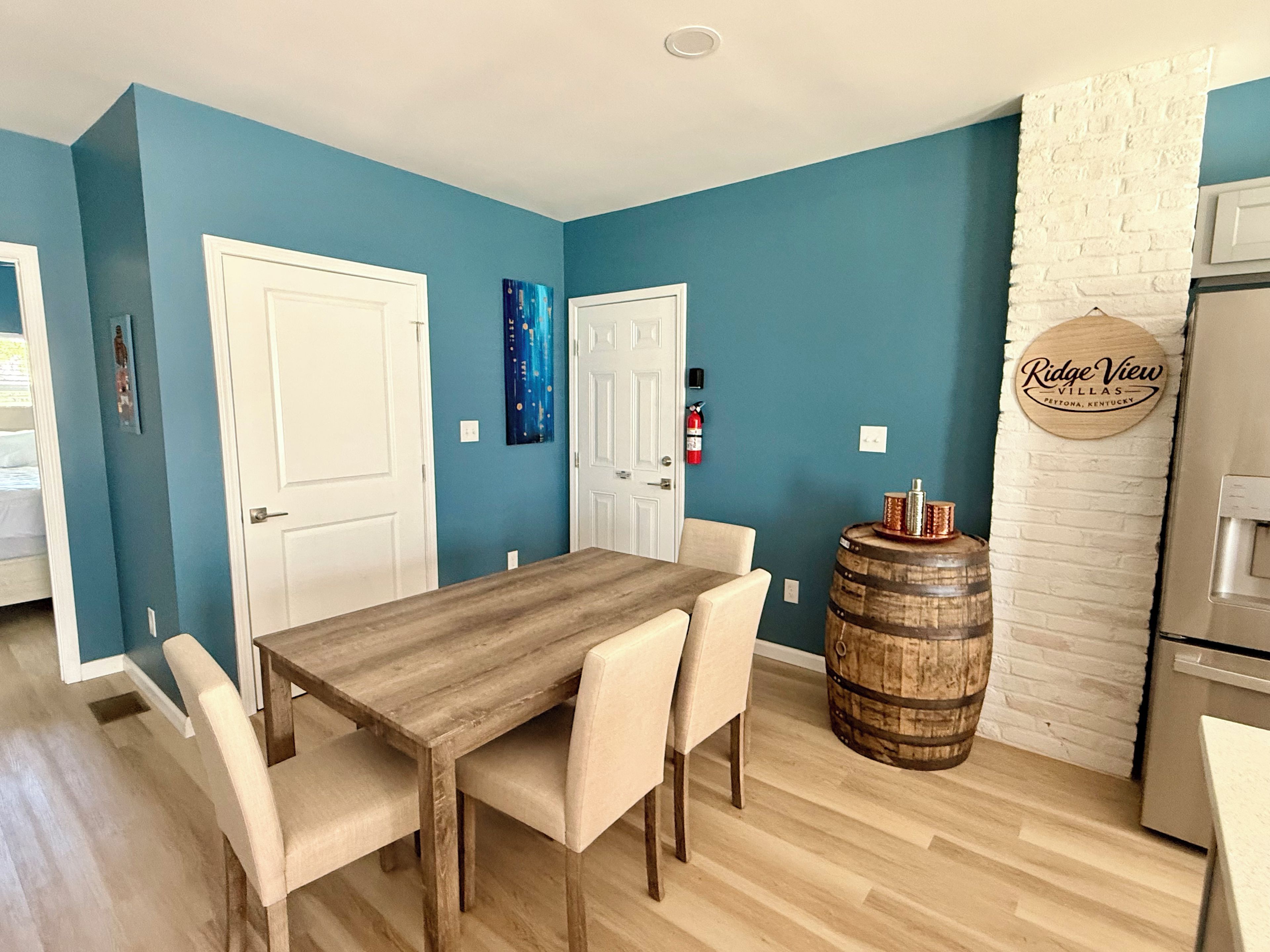 Un área de comedor con una mesa y sillas de madera, un barril y un cartel en una pared de ladrillo.
