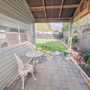 A covered patio area with a table and chairs, a view of a backyard with a lawn and a wooden fence.