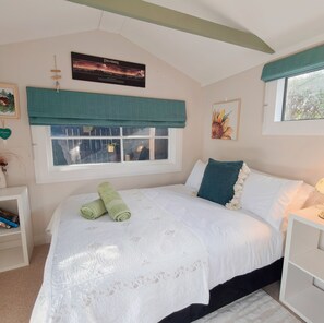 A bedroom with a bed, a window with a view, a painting on the wall, and a bedside table.