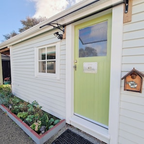 A small, single-story building with a green door, a window, and a sign indicating it is a guest room.