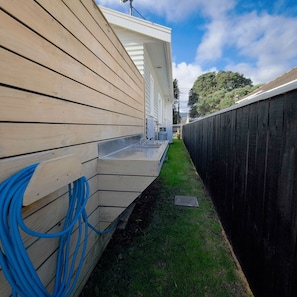 A wooden exterior wall with a gutter system and blue hoses. - The Garden Nest – A Boulcott Retreat (Lower Hutt)