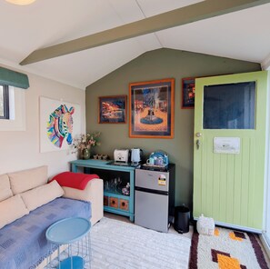 A compact living space with a kitchenette, a sofa, a small table, and a door labeled 'GUEST ROOM.' - The Garden Nest – A Boulcott Retreat (Lower Hutt)