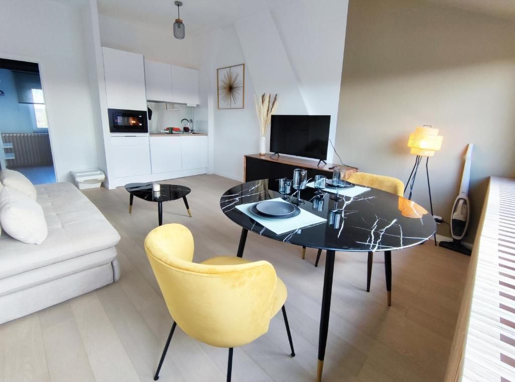 Een moderne woonkamer met een bank, gele stoelen, een eettafel met een zwart marmeren blad en een keuken op de achtergrond.