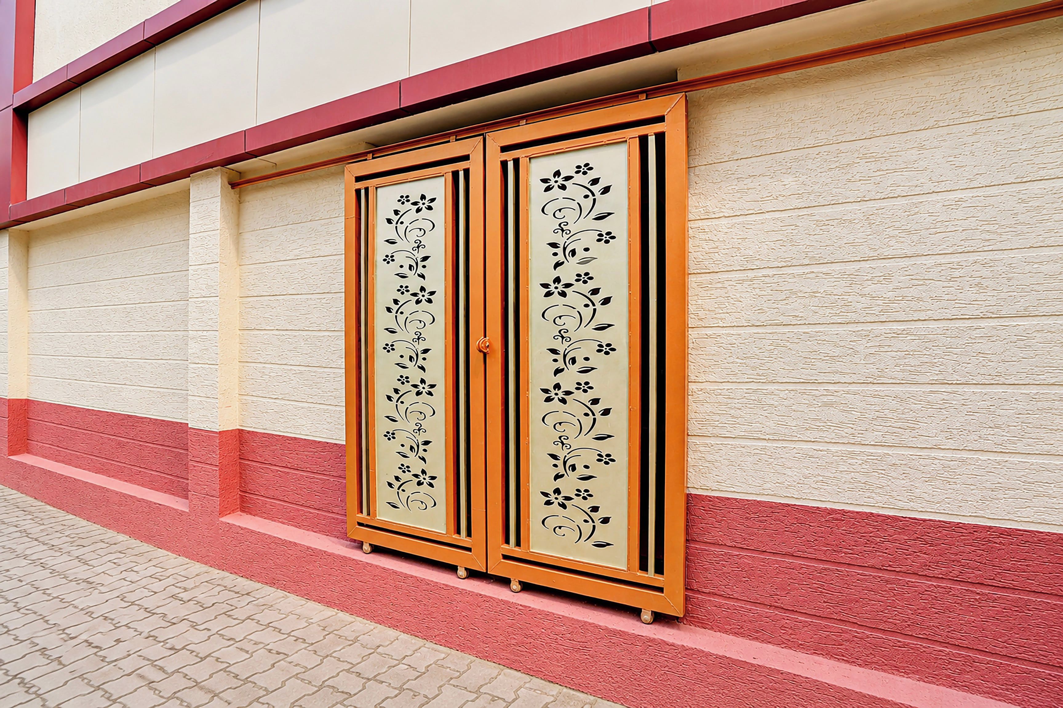 Fachada de edificio con pared texturizada en rojo y blanco, zócalo rojo y una puerta con panel decorativo.