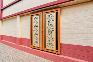 Fachada de edificio con pared texturizada en rojo y blanco, zócalo rojo y una puerta con panel decorativo.