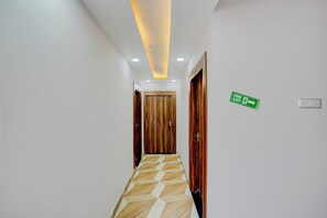 A hallway with a geometric patterned floor, wooden doors, and a green fire exit sign. - Townhouse Oak Banaras Station (Varanasi)