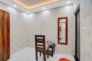 Una habitación con papel tapiz estampado, una silla de madera, una mesita con un hervidor y un espejo en la pared.