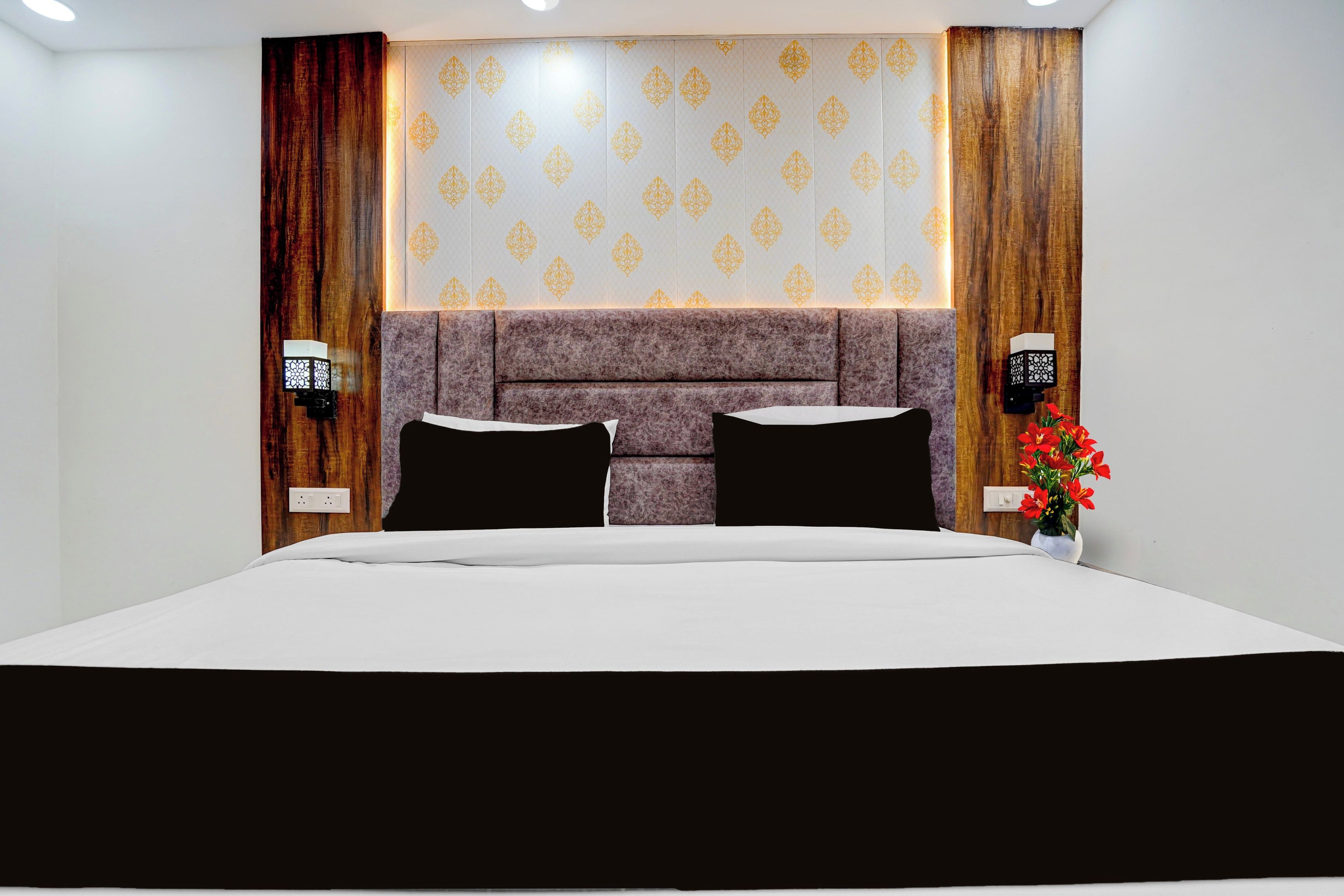 A hotel room with a large bed, a headboard with a patterned design, and two wall-mounted light fixtures.