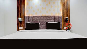 A hotel room with a large bed, a headboard with a patterned design, and two wall-mounted light fixtures.