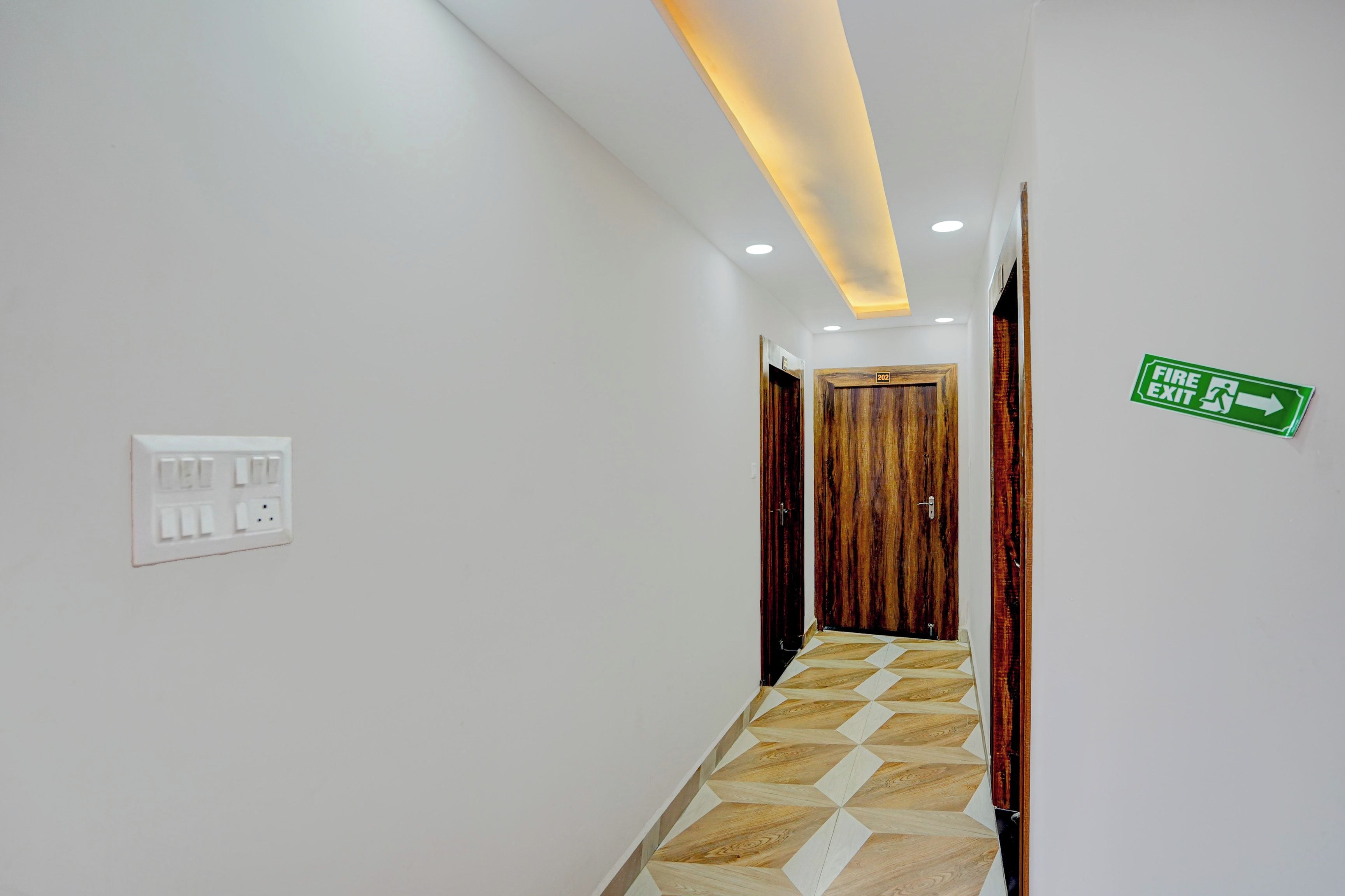 A hallway with a wooden door, a fire exit sign, and a light switch on the wall.