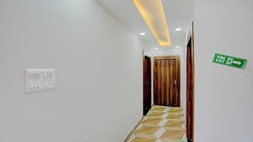 A hallway with a wooden door, a fire exit sign, and a light switch on the wall.