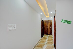 Un pasillo con puerta de madera, señal de salida de incendios y un interruptor de luz en la pared.