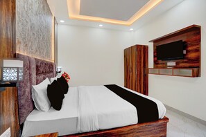A bedroom with a bed, a TV mounted on the wall, and a wooden headboard. - Townhouse Oak Banaras Station (Varanasi)