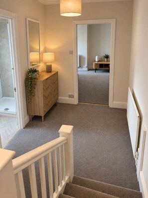 A hallway with a wooden dresser, a mirror, and a plant. There is a staircase with a white railing leading to another room. - The Lime Kiln (Oswestry)