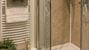 Un box de ducha moderno con puerta de cristal, un perchero con toallas dobladas e impresión botánica enmarcada en la pared.