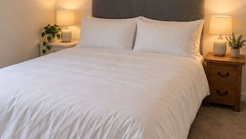 A bedroom with a bed, two bedside tables, a nightstand, and two wall-mounted pictures.
