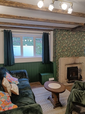 A cozy room with a green upholstered sofa, a small round table, a fireplace, and a window with curtains.