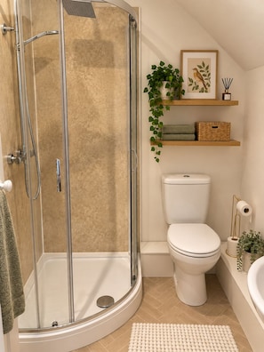 Un baño moderno con ducha de vidrio, inodoro, bañera y un estante pequeño con una planta y un marco de fotos.