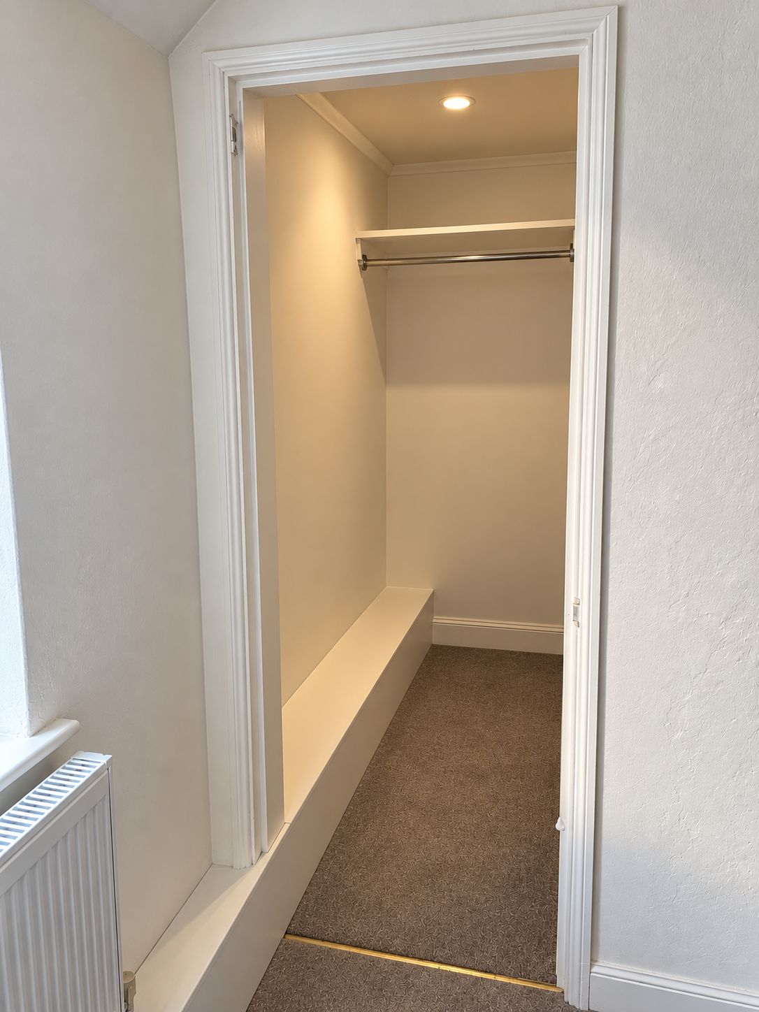 A narrow hallway with a radiator, a bench, and a door leading to a room.