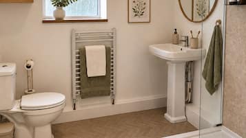 A bathroom with a toilet, sink, and shower. There are framed botanical prints on the wall, a radiator, and a window with a plant.