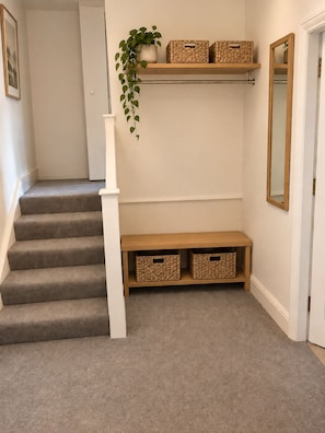 A staircase with a white handrail, a small bench with baskets, and a plant on the wall.