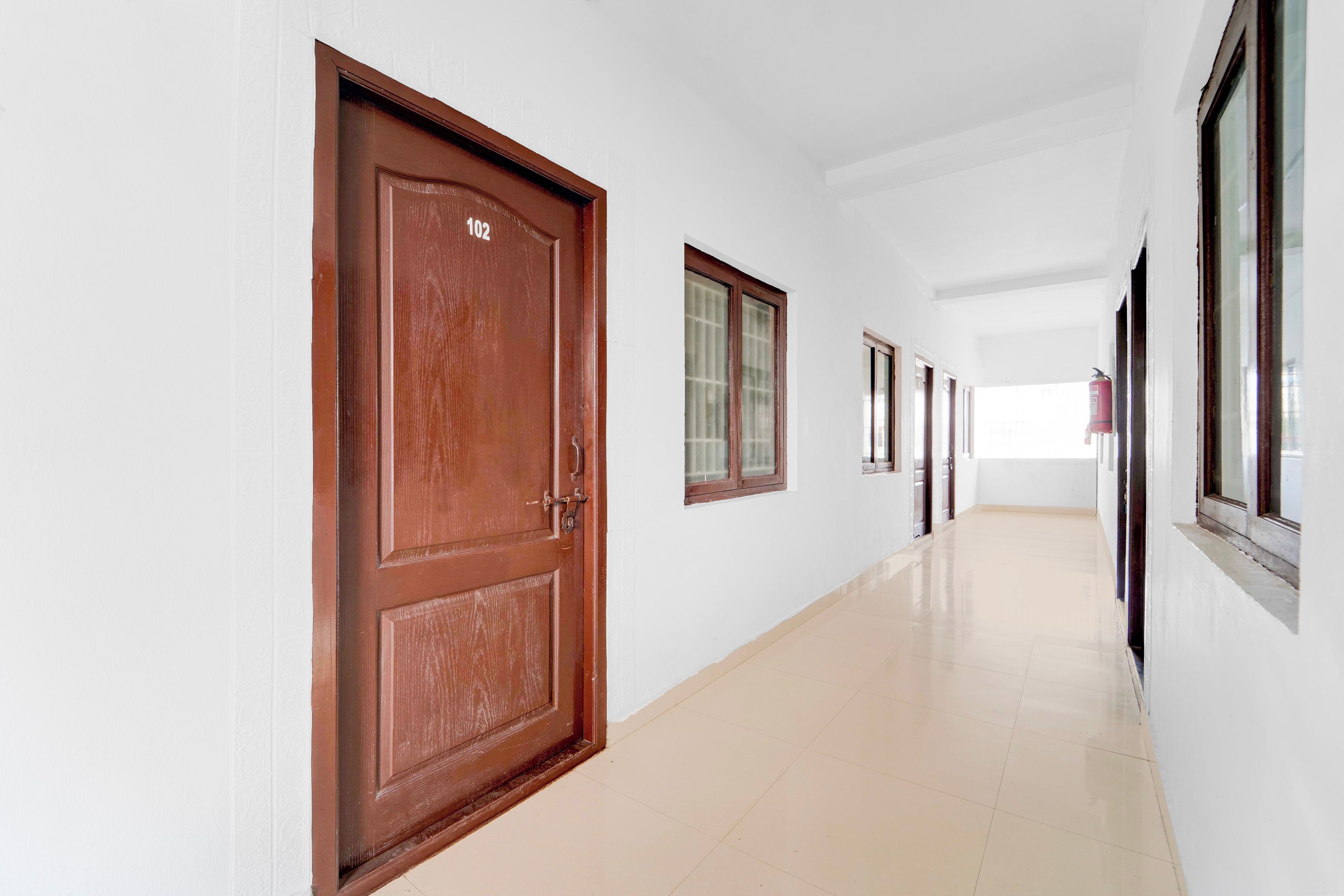 Un pasillo con puertas y ventanas de madera, suelo de baldosas y un extintor en la pared.