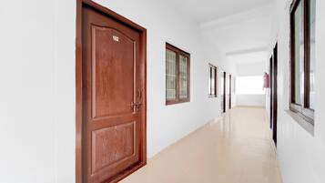 Un pasillo con puertas y ventanas de madera, suelo de baldosas y un extintor en la pared.