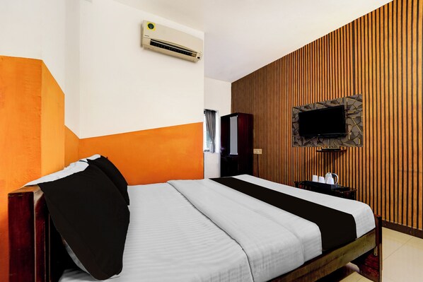 A hotel room with a bed, a flat-screen TV mounted on a wooden wall, and an air conditioning unit on the wall.