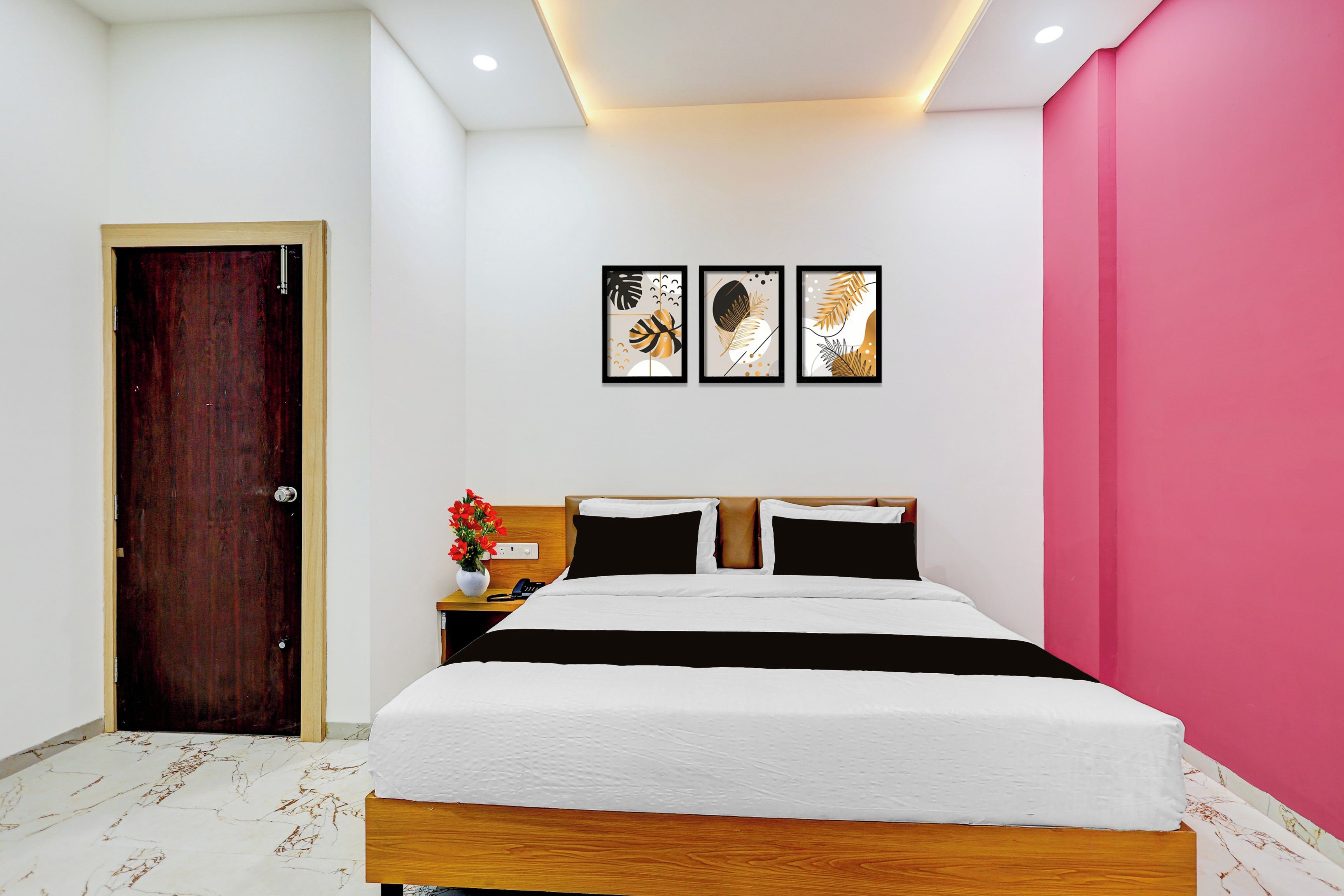 Habitación de hotel con cama de madera, mesita de noche con teléfono y tres cuadros en la pared.