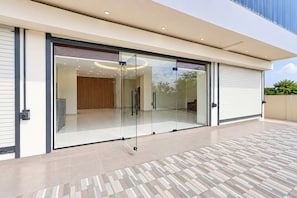Um edifício moderno com grandes portas de vidro deslizantes, piso ladrilhado e interior visível, com porta de madeira e lustre.