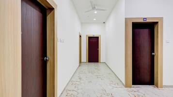 Un pasillo con puertas de madera, un ventilador de techo y piso de mármol.