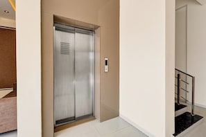 Un ascensor moderno con detalles metálicos, un panel de control y una escalera con barandilla negra.