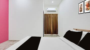 Una habitación de hotel con cama, ventana con cortinas, equipo de aire acondicionado y una pared decorada con obras enmarcadas.