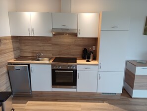 Eine kompakte Küche mit Geschirrspüler, Herd, Backofen und Kaffeemaschine auf der Arbeitsplatte.