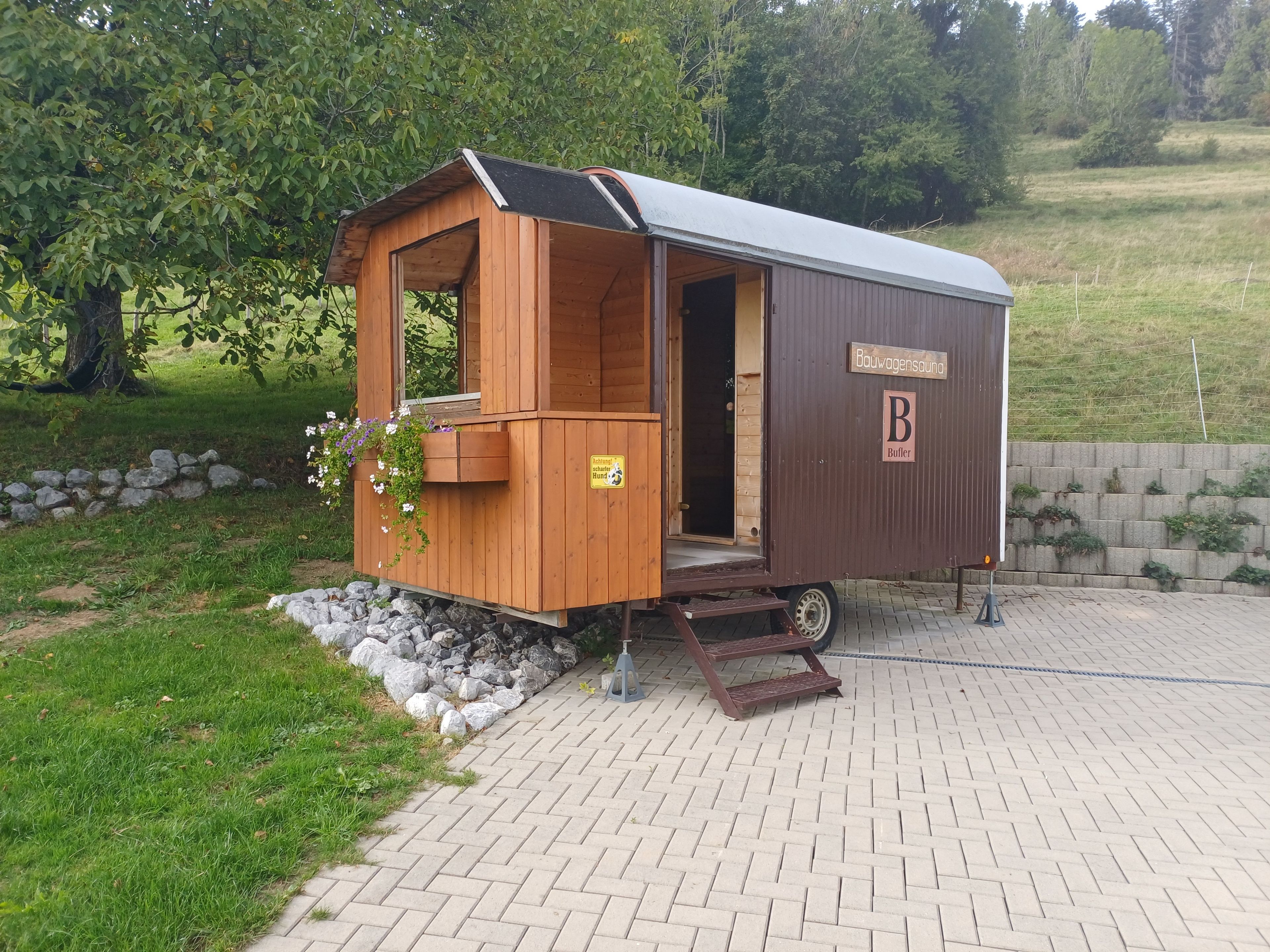 Ein Wohnmobil aus Holz mit überdachter Veranda und einem Schild, das es als 'Bauwagenhaus' kennzeichnet.